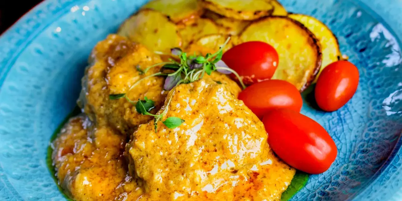 Köttbullar i krämig cafe de paris sås med rostade potatisskivor och körsbärstomater på en blå tallrik.