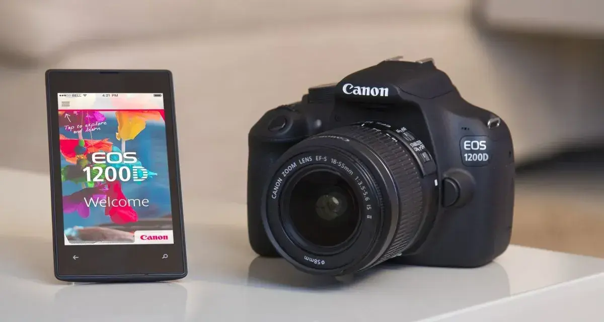 Czarny aparat cyfrowy Canon EOS 1200D obok smartfona z aplikacją powitalną.