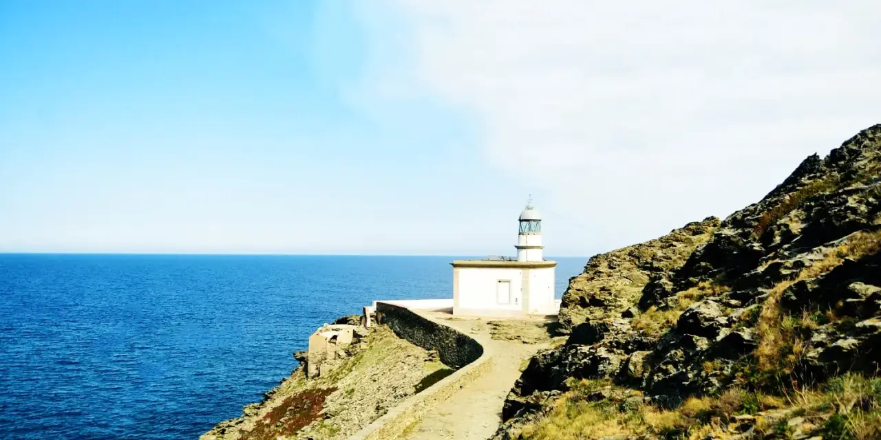 El faro de Cala Nans se alza sobre un acantilado rocoso, vigilando el azul intenso del mar Mediterráneo bajo un cielo despejado.