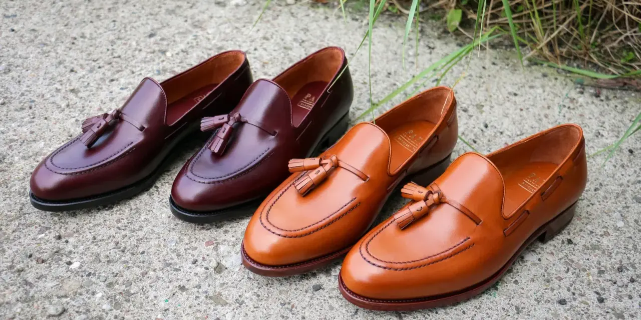 Eleganckie, skórzane loufersy z chwostami w kolorze koniaku i burgundu, ułożone na betonowej nawierzchni.