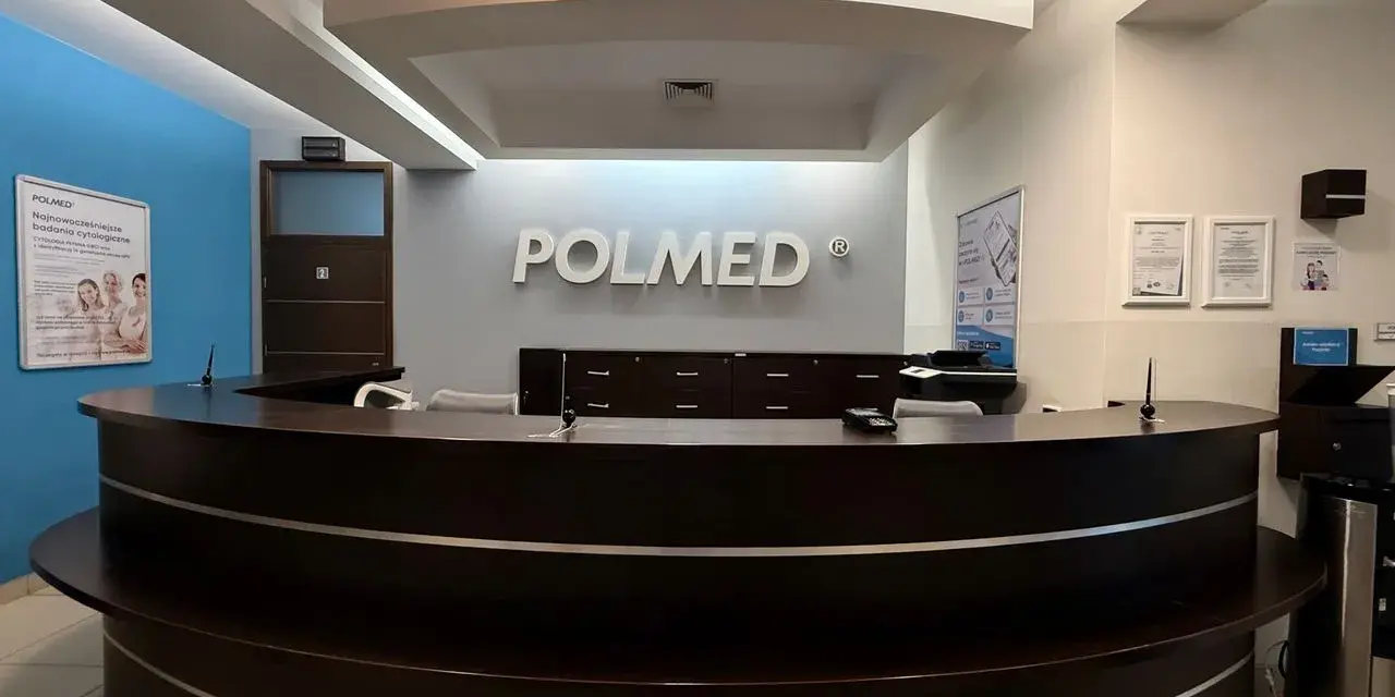 Recepcja kliniki medycznej POLMED z ciemnobrązowym ladą i logo na ścianie.