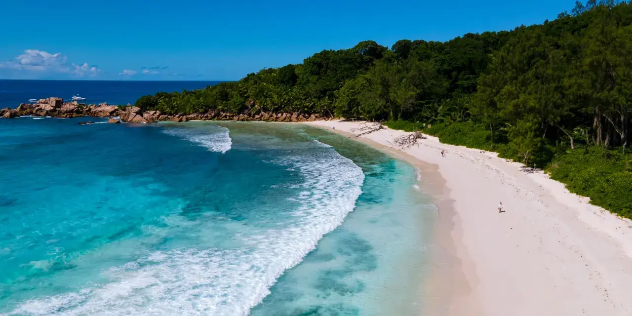 Rajska wyspa na Oceanie Indyjskim. Turkusowa woda obmywa piaszczystą plażę, a bujna zieleń porasta wzgórza.