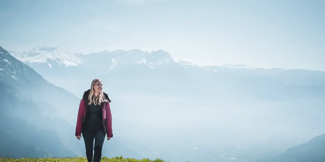 Frau in Wanderkleidung genießt die Aussicht auf verschneite Berge. Perfekt, was zieht man zum wandern an!