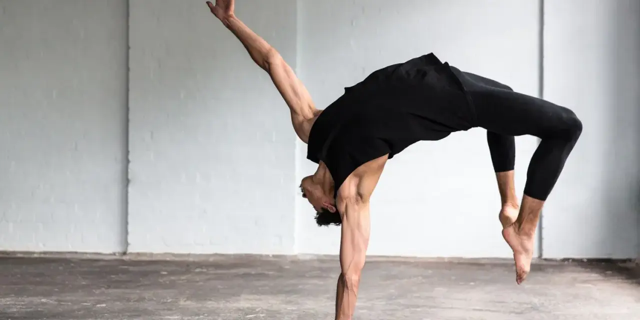Un bailarín en un estudio blanco realiza un movimiento acrobático, mostrando que es la danza.