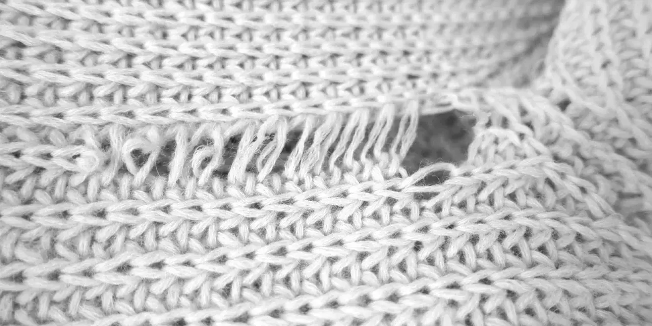 Nahaufnahme eines weißen Strickpullovers mit einem Loch und ausgefransten Fäden. Was tun, wenn die Wolle eingelaufen ist?