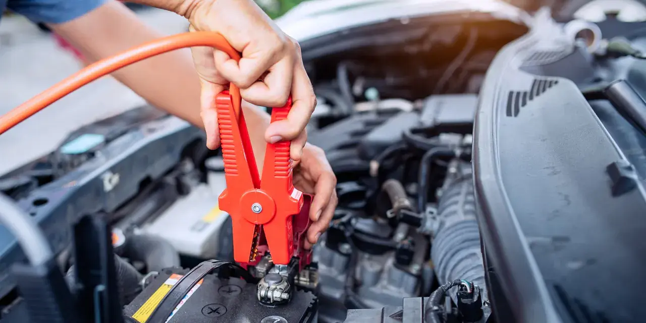 Hands connect jumper cables to a car battery, a common fix when wondering how long can a car be on before the battery dies.