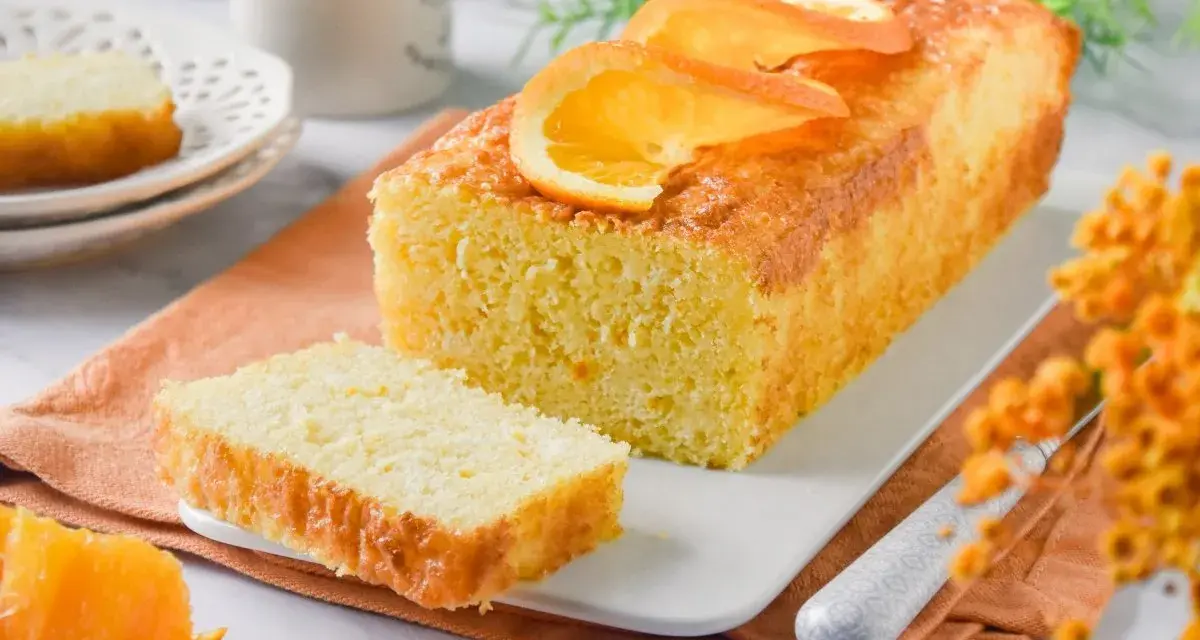 Un delicioso bizcocho de naranja, recién horneado y decorado con rodajas de naranja. Perfecto para acompañar un café.