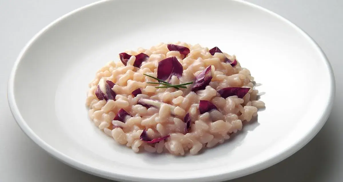 Un cremoso risotto al radicchio rosso, guarnito con erba cipollina, servito su un piatto bianco.
