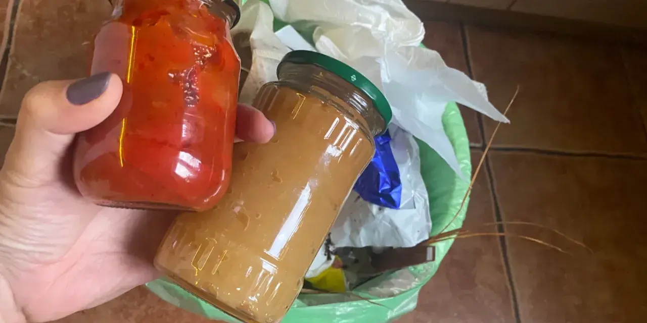 Dwie słoiki z przetworami, jeden z papryką, drugi z dżemem, trafiają do kosza. Tak wygląda prawidłowe wyrzucanie starych przetworów.