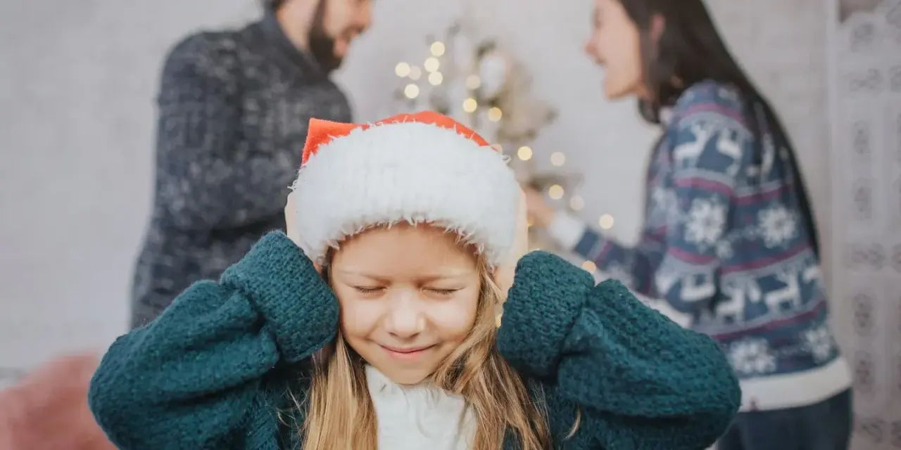 Ein Kind mit Weihnachtsmütze hält sich die Ohren zu, während die Eltern im Hintergrund streiten. Weihnachten trennen sie.