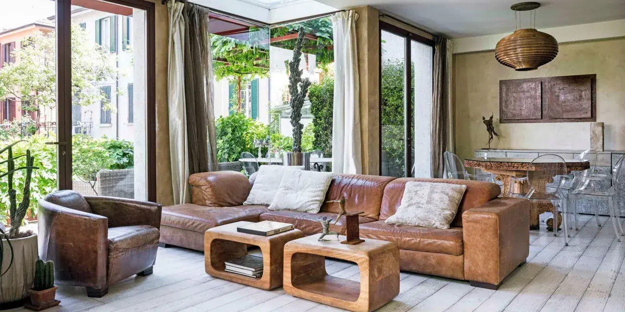 Accogliente soggiorno etnico chic con divano in pelle, poltrona vintage e vista sul verde.