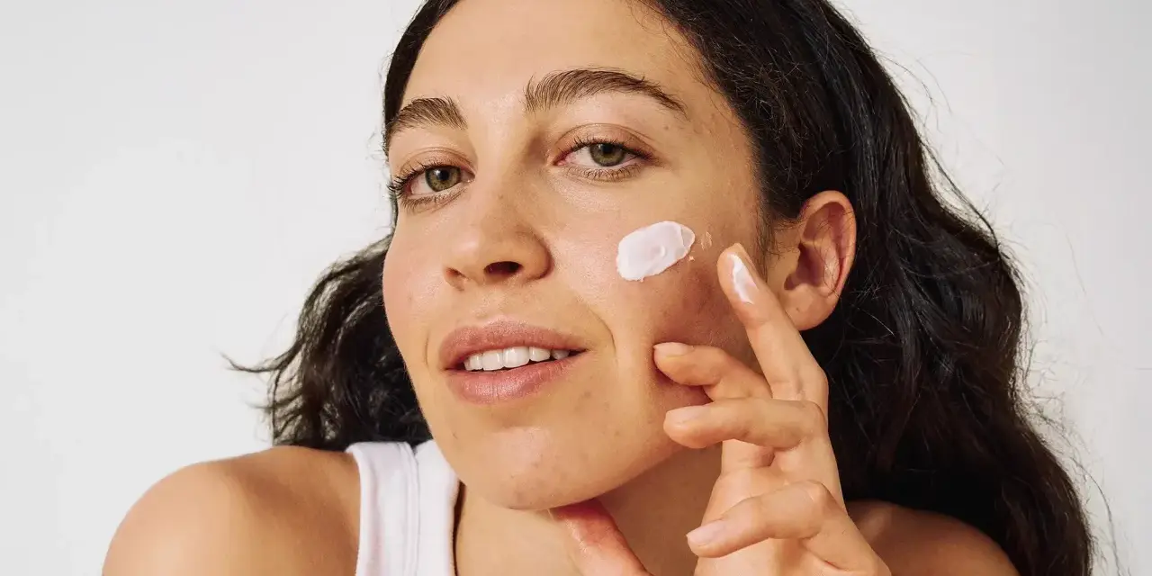 Frau mit zu Akne neigender Haut trägt eine leichte Creme auf.
