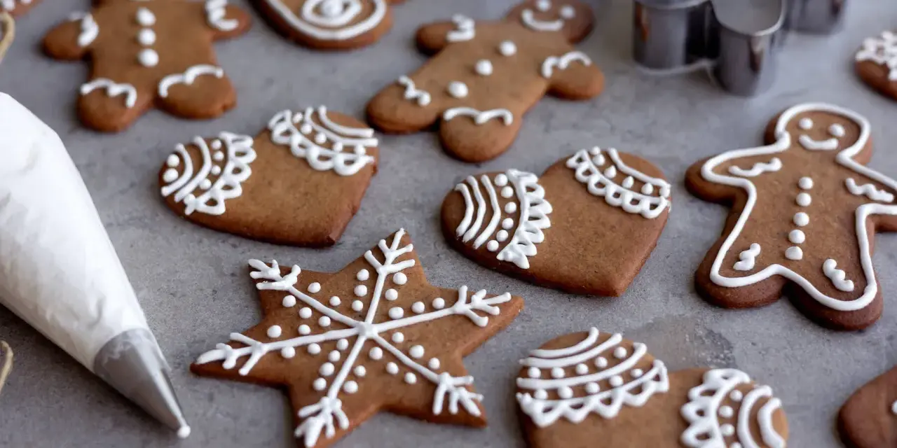 Pepparkakshus och hjärtan dekorerade med vit kristyr. En sprits med kristyr ligger bredvid.