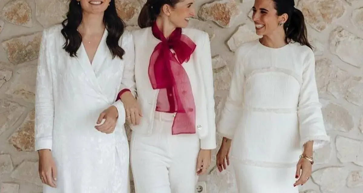 Tres mujeres sonríen vestidas de blanco, demostrando que se puede ir de blanco a un bautizo.