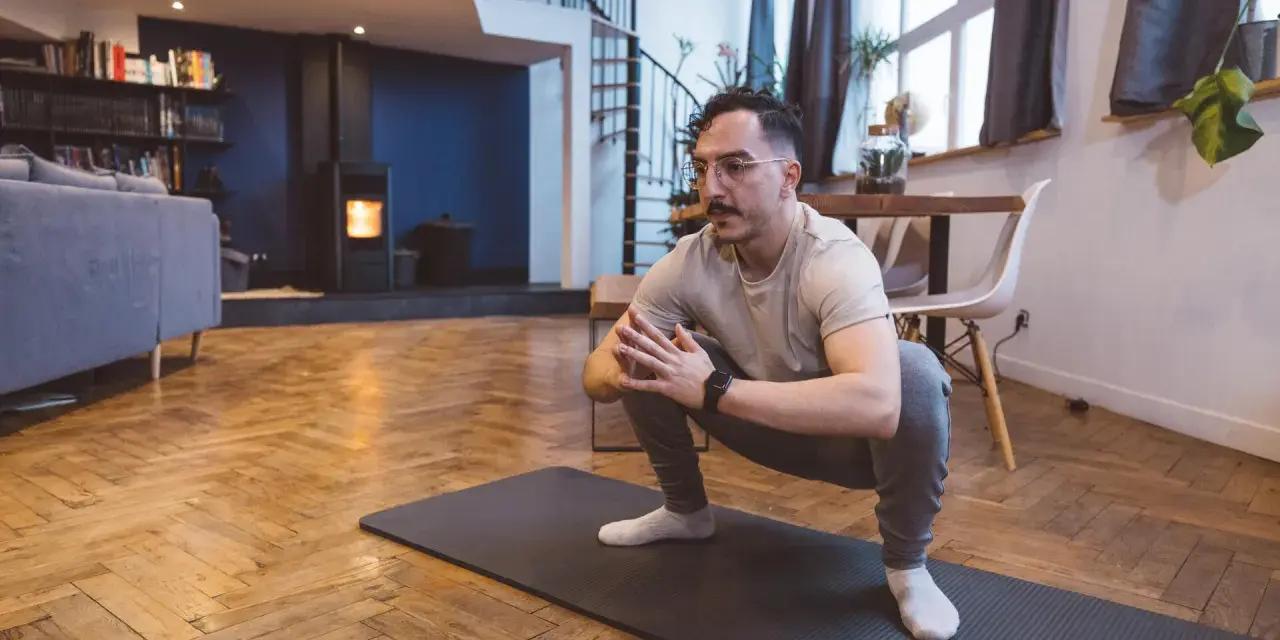 Homme en tenue de sport effectuant un étirement pubalgie sur un tapis de yoga dans un salon moderne.