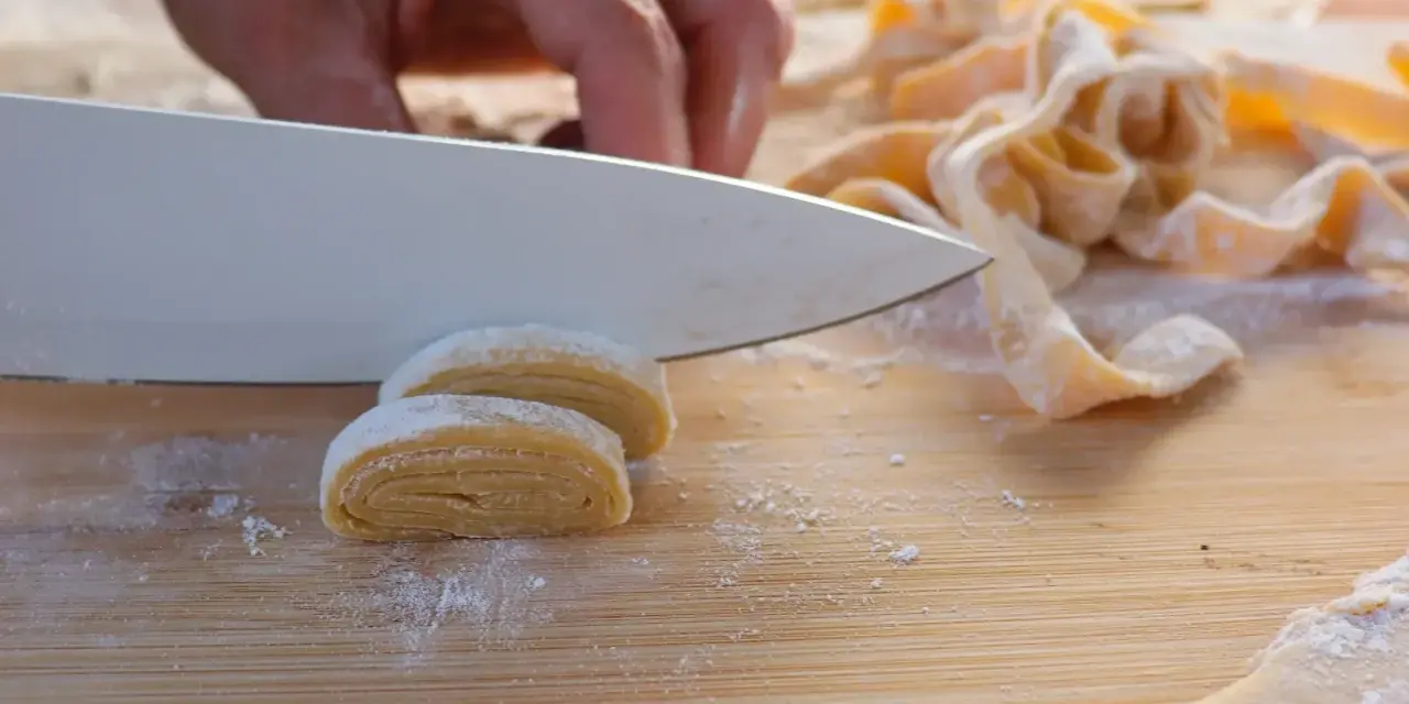 Hand schneidet frisch zubereitete, selbstgemachte Pasta auf einem Holzbrett.