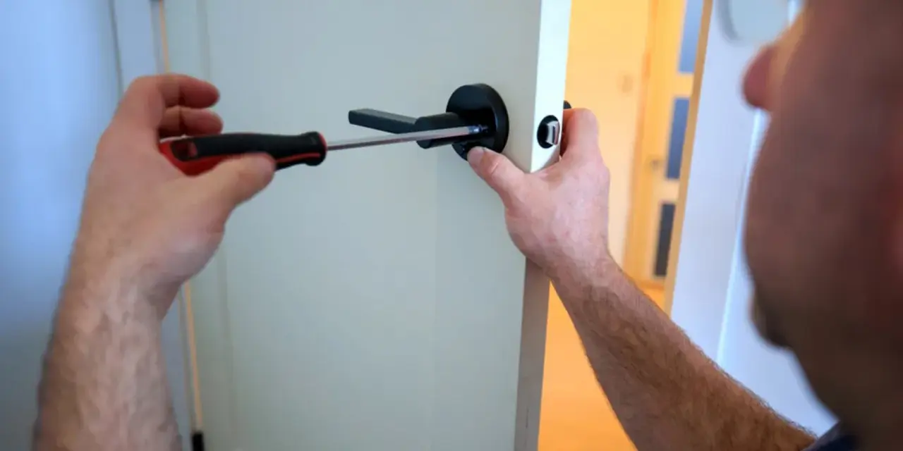 Un homme utilise un tournevis pour fixer une poignée de porte noire. Il est sur le point de lever la poignée pour fermer la porte.