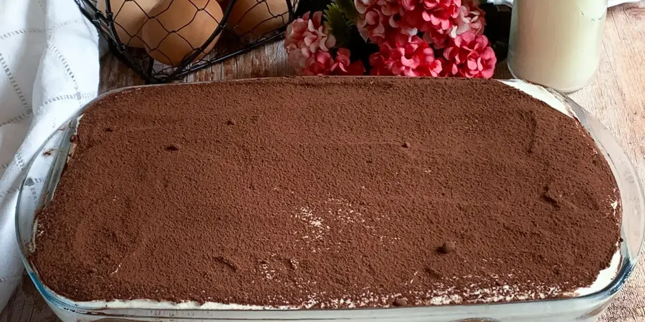 Tiramisù pronto, con 250 gr di mascarpone, pronto per essere gustato. Ingredienti freschi come uova e fiori decorano la tavola.