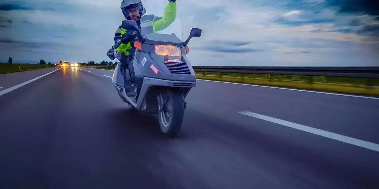 Karta motorowerowa w akcji! Kierowca w kasku i kamizelce odblaskowej pozdrawia, jadąc skuterem po autostradzie.