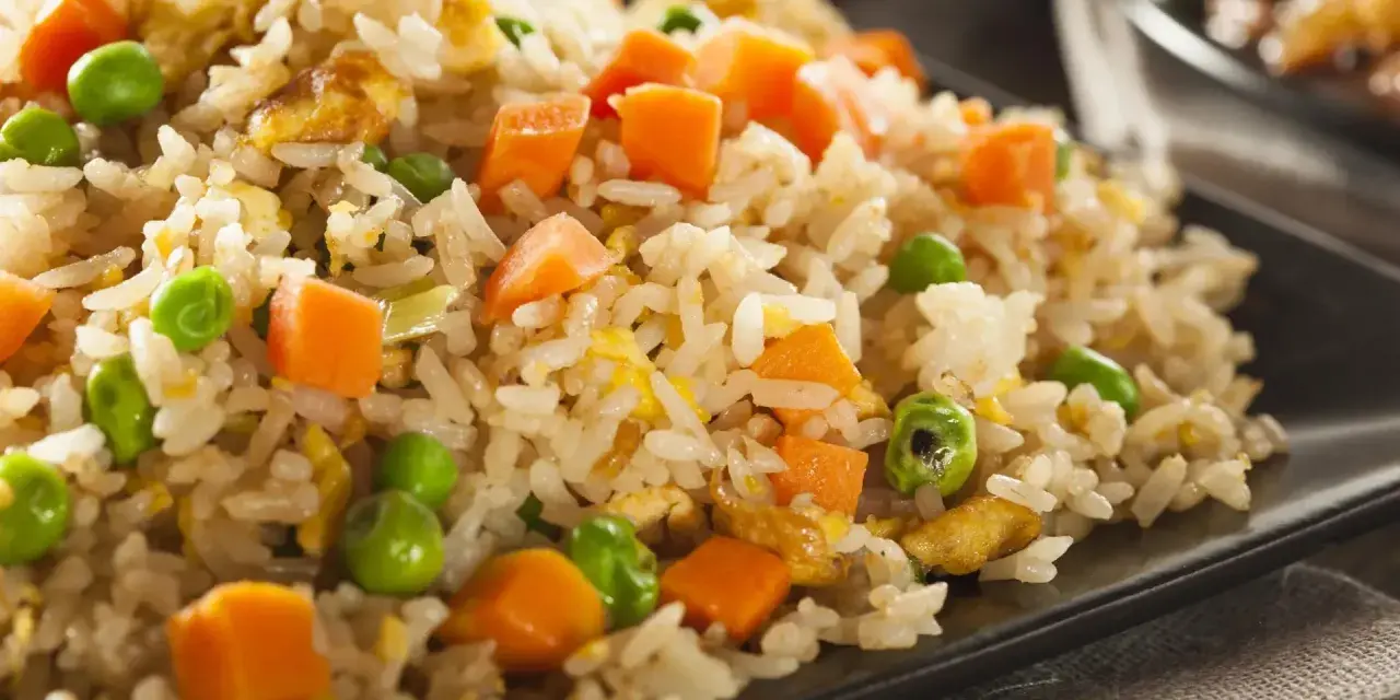 Arroz tres delicias con guisantes y zanahoria en un plato negro.