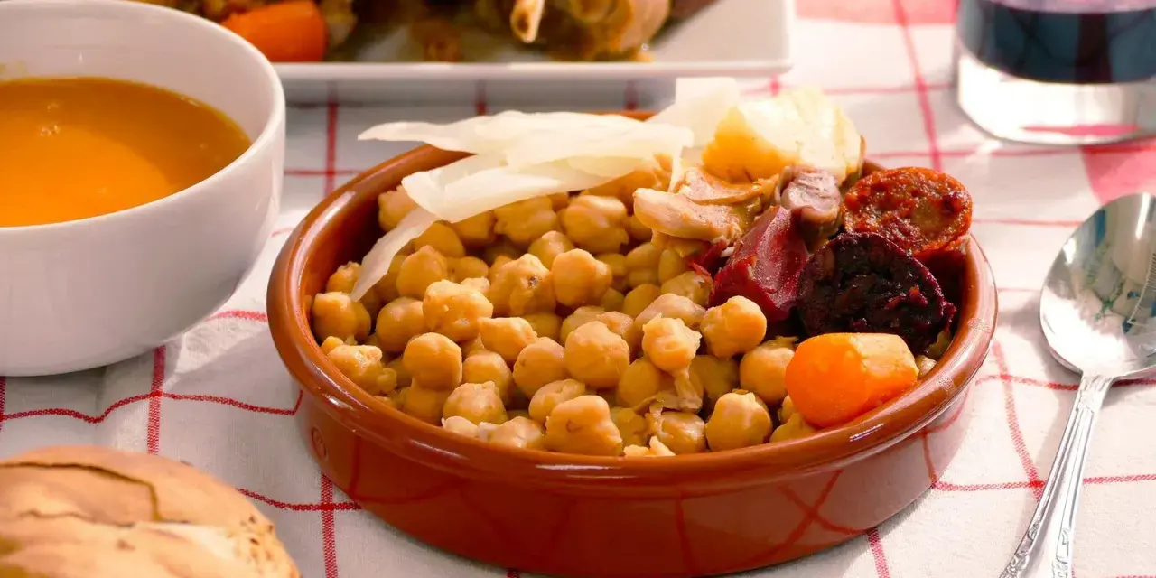 Cocido madrileño con garbanzos, chorizo, morcilla, patata y zanahoria en cuenco de barro.