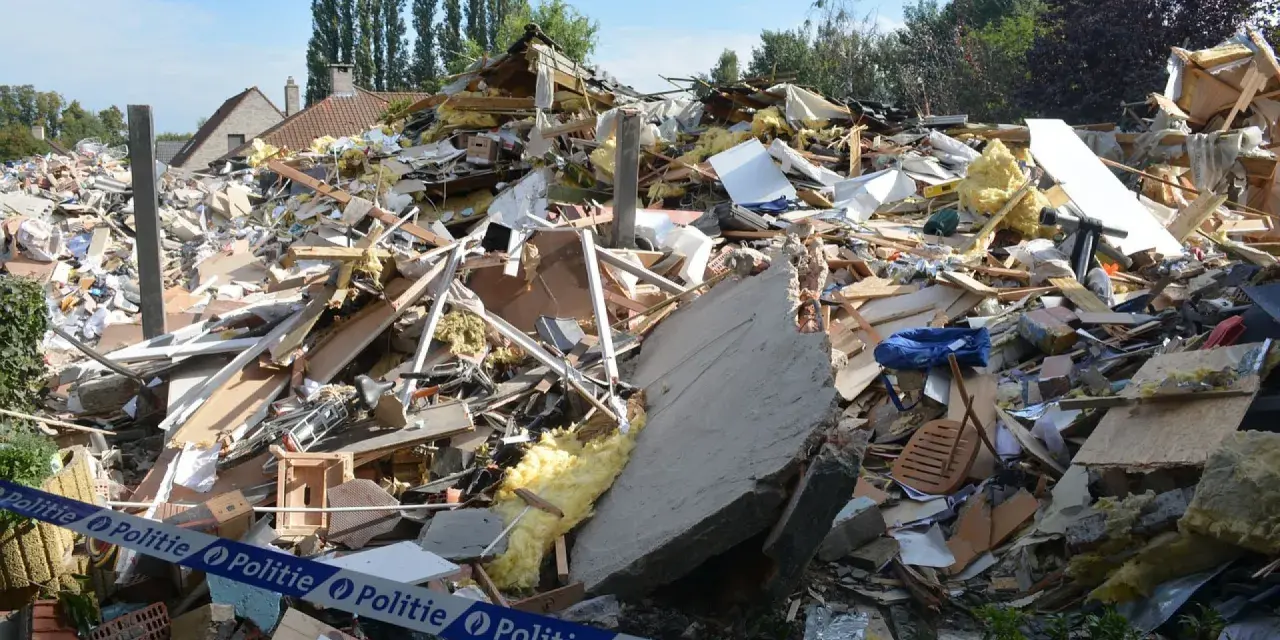 Ogromna kupa gruzów po zawaleniu się budynku. Widać izolację, drewno, beton i niebieską torbę. Wstęga policyjna zabezpiecza teren.