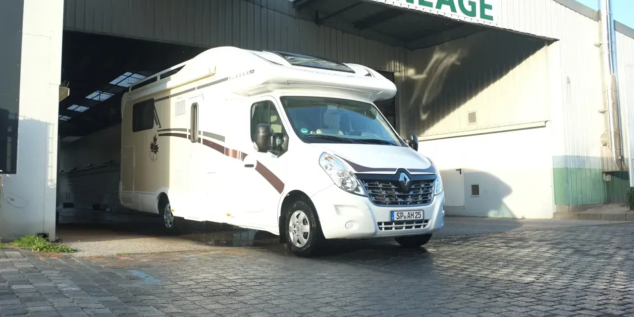 Biały kamper Alaska TD wyjeżdża z zadaszonego miejsca, gotowy na przygodę. Idealny na rodzinny camper park.