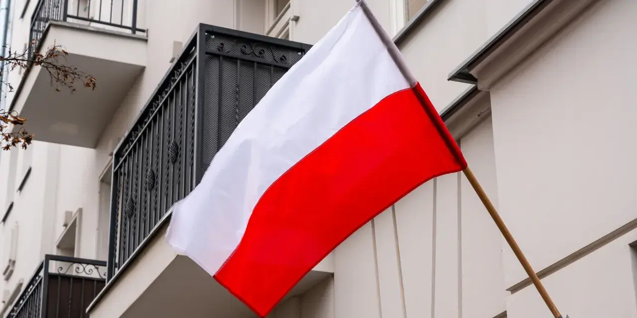 Flaga Polski w pionie, biało-czerwona, powiewa na tle budynku z balkonem.