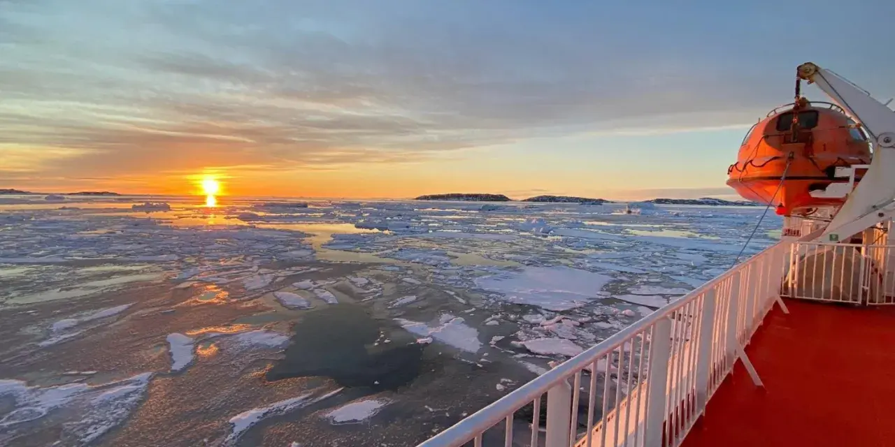A **Greenland ferry** navigates icy waters at sunset. An orange lifeboat hangs ready on the ship's deck.
