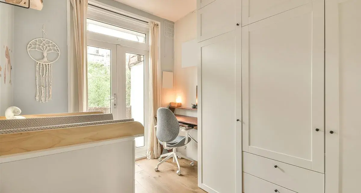 Un angolo studio in camera da letto, con scrivania, sedia girevole e armadio bianco.