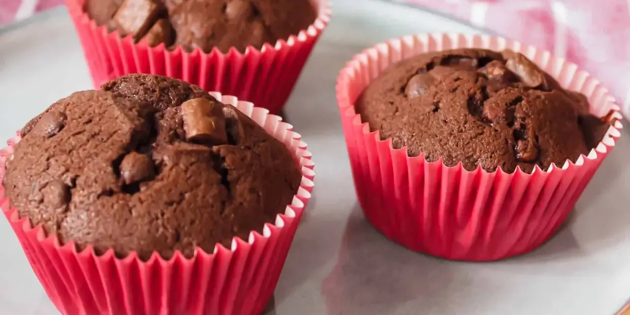 Drei saftige Schokomuffins mit Schokostückchen in roten Papierförmchen, perfekt für Kinder.
