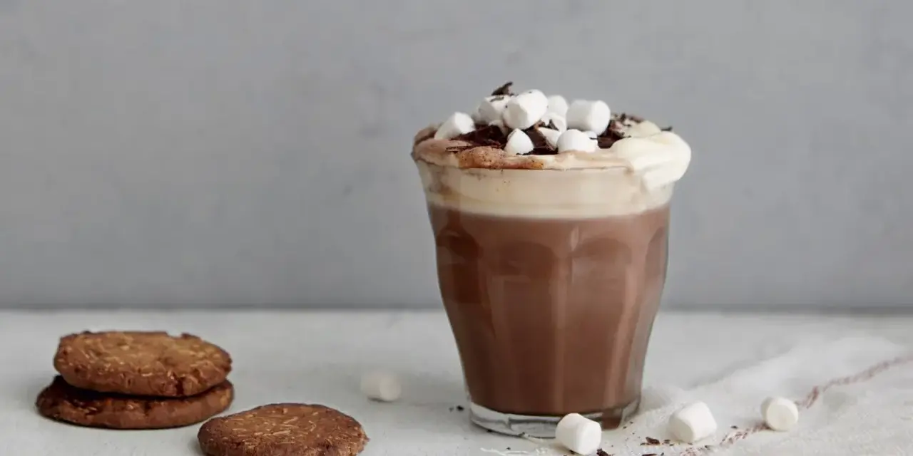 En härlig varm choklad med choklad, toppad med marshmallows och chokladspån. Bredvid står några chokladkakor.