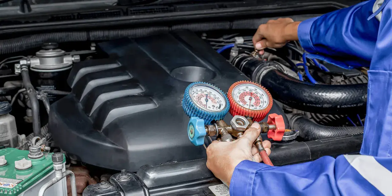 Mecánico realiza carga de gas al aire acondicionado de un coche, usando manómetros para verificar la presión.