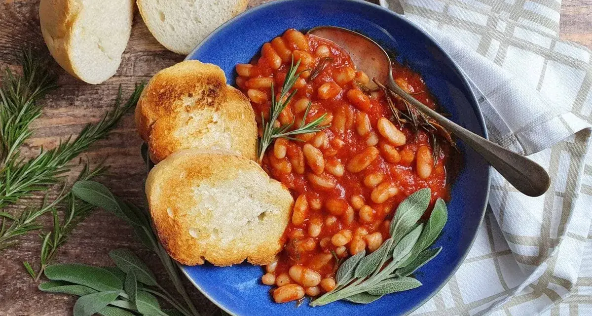 Fagioli all'uccelletto in umido con pomodoro, serviti con pane tostato e erbe aromatiche. Perfetti per scoprire cosa abbinare ai fagioli all'uccelletto.