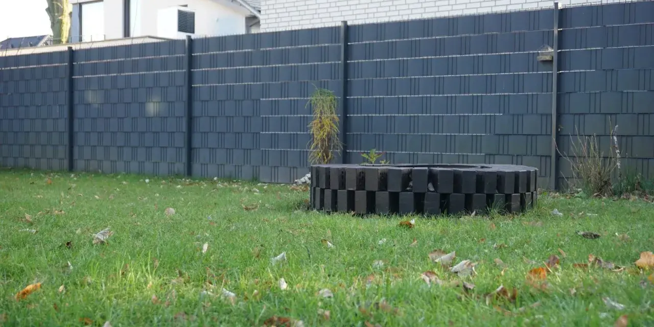 Moderner Sichtschutzzaun, der sich gut zum zaun selber bauen billig eignet. Ein dekorativer Kreis aus schwarzen Steinen im Garten.