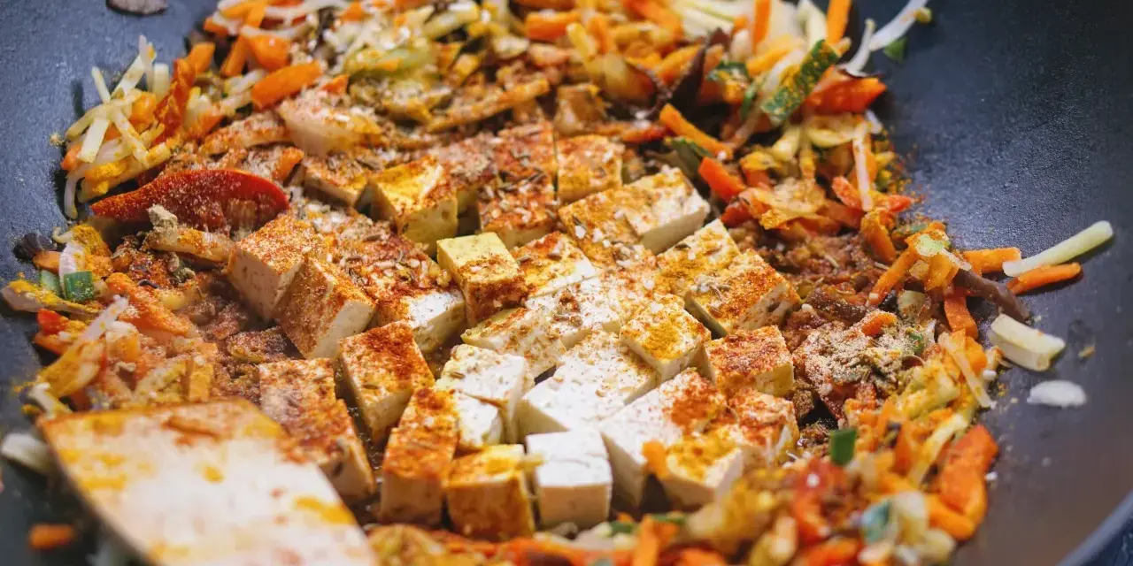 Kawałki tofu i kolorowe warzywa po chińsku smażą się na patelni wok, przyprawione kurkumą i papryką.