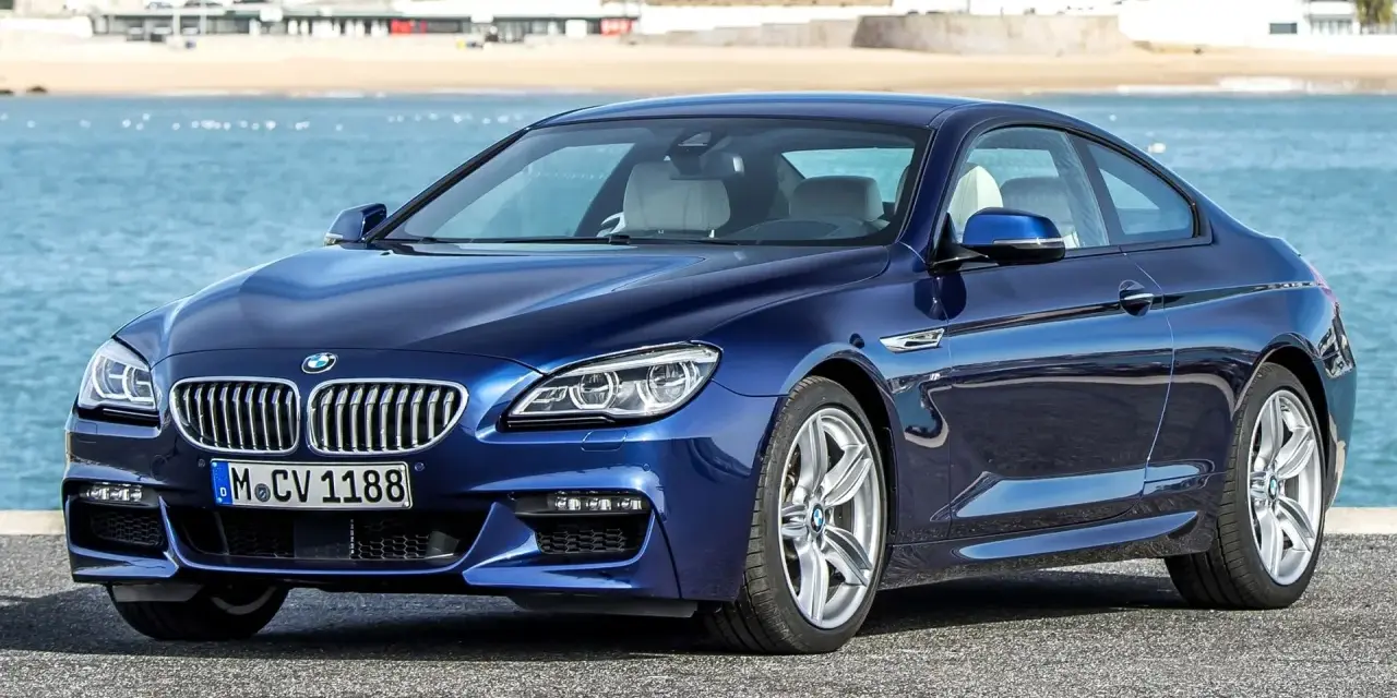 Granatowe BMW 640d coupe z jasnym wnętrzem zaparkowane nad błękitnym morzem, w tle zabudowania nadbrzeżne.