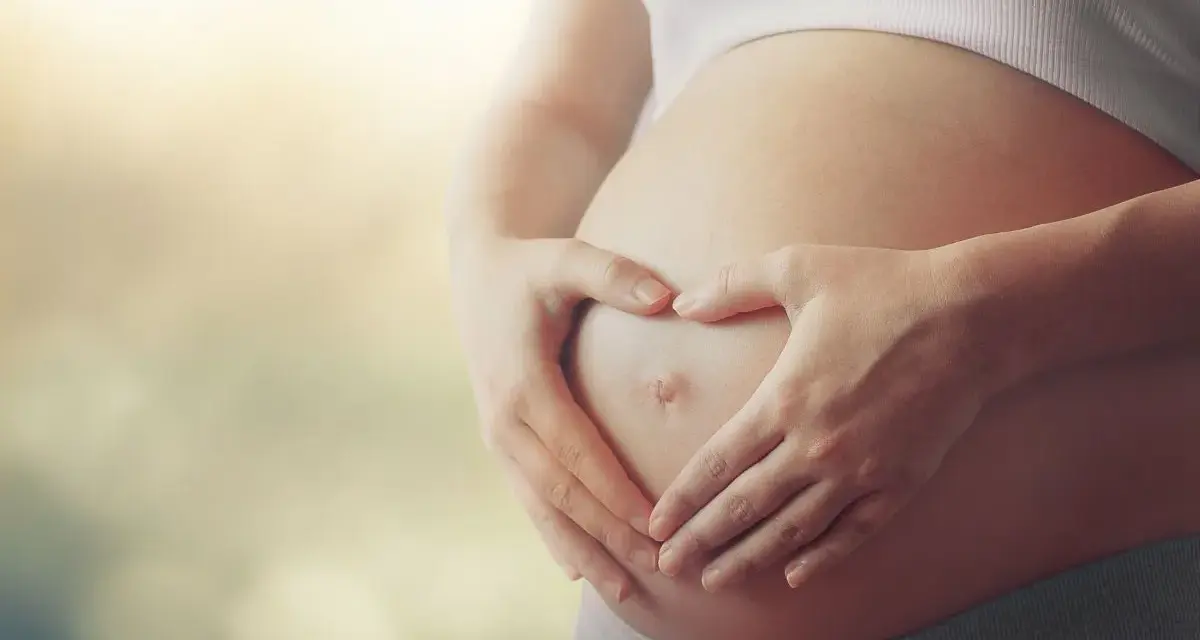 Czekając na dziecko, zastanawiasz się, czy autyzm można wykryć w ciąży? Dłonie tworzą serce na brzuchu.