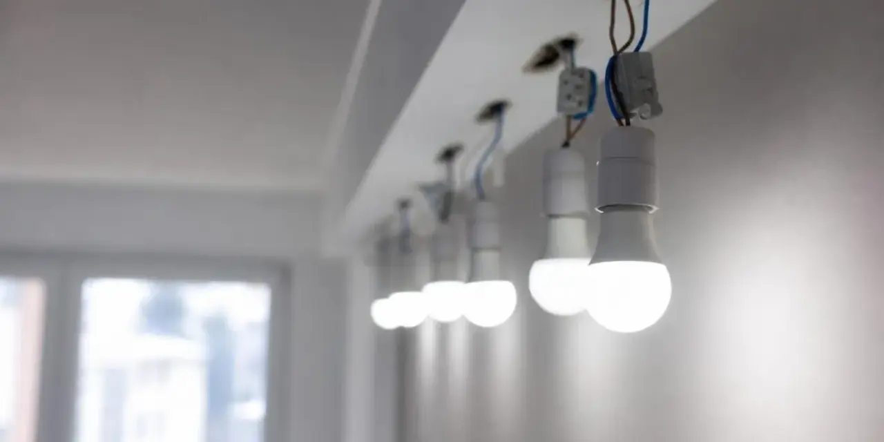 Rząd białych żarówek LED, wiszących na przewodach, świeci jasno, mimo że instalacja wygląda na nieukończoną.