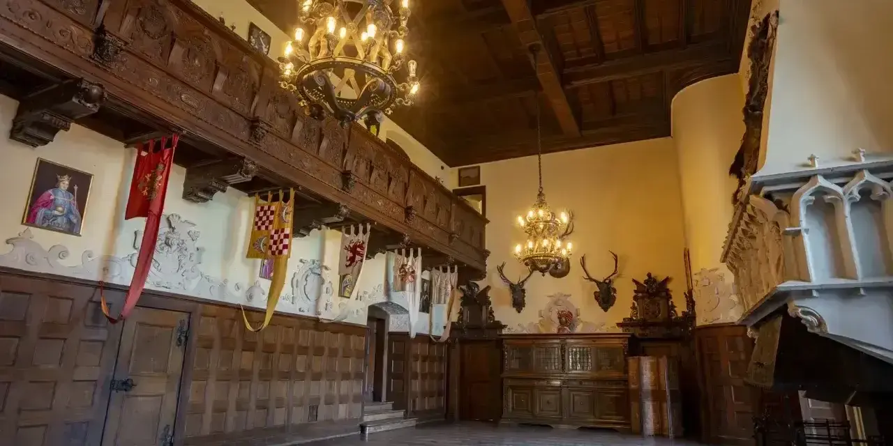 Wnętrze zamku Czocha z bogatymi zdobieniami, portretem króla i banerami. Bilety do zamku czekają na odkrycie jego historii.