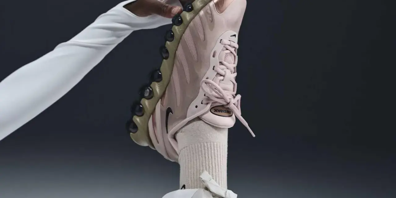 Różowy but Nike na obcasie, trzymany przez dłoń w białej rękawiczce.