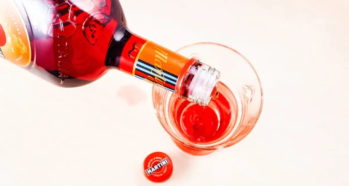 Czerwony Martini Fiero drink nalewany z butelki do szklanki. Obok leży czerwona zakrętka z logo Martini.