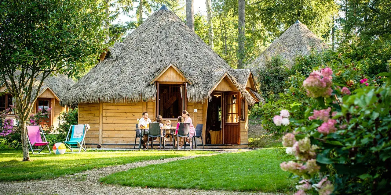 Famille profitant d'un repas en terrasse devant leur chalet en chaume, parfait pour des vacances scolaires en Bretagne.