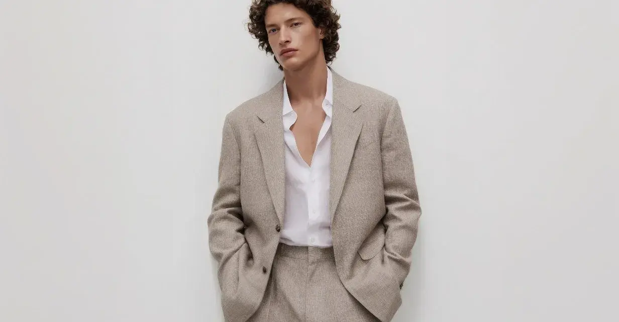 Uomo con capelli ricci indossa un completo beige, incarnando l'eleganza discreta dell'old money significato.