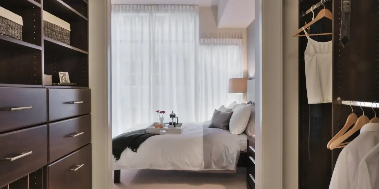 Dormitorio con vestidor integrado. Un espacio organizado con estanterías oscuras y cajones, que da paso a una cama acogedora y un armario con ropa colgada.