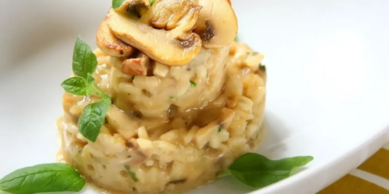 Kremowe risotto z grzybami, udekorowane listkami bazylii i oregano, prezentuje się apetycznie na białym talerzu.