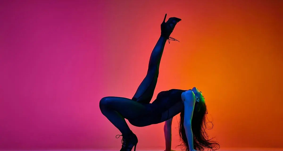 Tancerka w czarnym body i szpilkach wykonuje akrobatyczną figurę na tle gradientu różu i pomarańczy. High heels co to? To buty, które dodają pewności siebie.