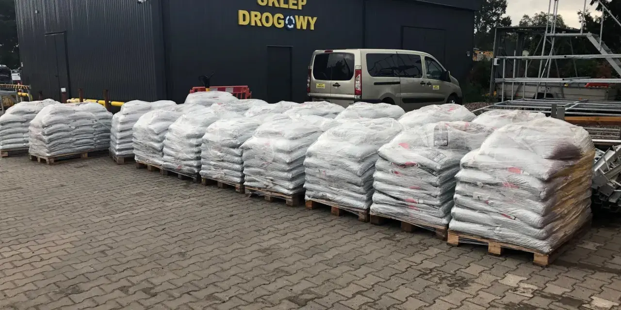 Palety z workami materiałów budowlanych przed sklepem drogowym.