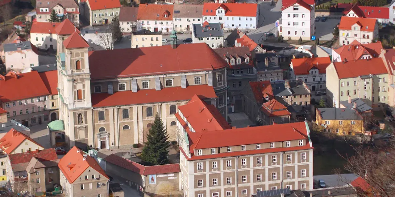 Widok z góry na miasteczko z czerwonymi dachami, w centrum imponujący kościół i zabudowania. To urokliwe bardo śląskie.