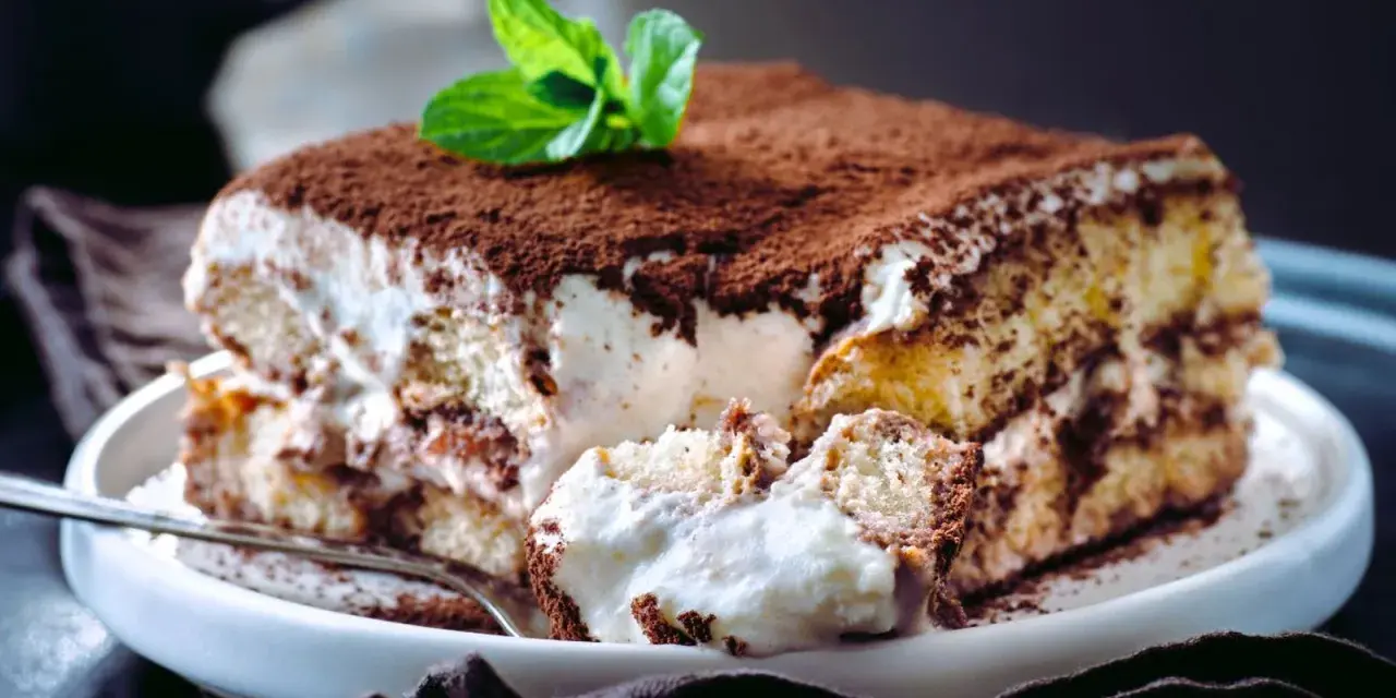 Tiramisú cremoso cubierto de cacao y decorado con menta.